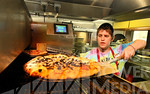 Kaleb Aduddell gets a pizza out of the oven at Hideway Pizza on Western Thursday. Oklahoma-based Hideaway offered 50 percent off all carryout orders when customers placed them online, except ...